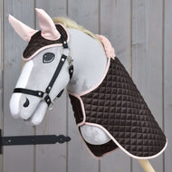 Zestaw Termo Sweety od Hobby Horse LarDen przedstawia pluszowego Hobby Horse z uzdą, ubranego w pikowaną brązowo-różową derkę i dopasowany nausznik, na tle drewna.