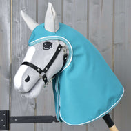 Płaszcz przeciwdeszczowy Turkusowy od Hobby Horse LarDen przedstawia szarego Hobby Horse z czarną uzdą i turkusowym kapturem w stylu płaszcza przeciwdeszczowego, z realistycznie ukształtowaną twarzą z czarno-białymi detalami, na tle jasnego drewna.