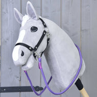 The Hobby Horse LarDen "Reins Viola" is a gray hobby horse with a white blaze, black bridle, and vibrant handmade reins, featuring a plush head on a sturdy stick and displayed against a light wooden fence.