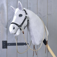 Szary pluszowy Hobby Horse od Hobby Horse LarDen, z rozdzielonymi wodzami western Dallas i czarną uzdą, osadzony na drewnianym kiju przed szarą drewnianą ścianą.