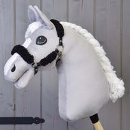Hobby Horse LarDen z czarnym kantarem z pełnym czarnym futerkiem ze skóry ekologicznej i drewnianym kijem, pokazany na tle drewnianych paneli.