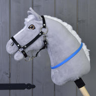 Hobby Horse Cordeo niebieski (rozmiar S) od Hobby Horse LarDen przedstawia szare pluszowe ciało, białą grzywę, czarną uzdę i niebiesko-fioletową wstążkę na drewnianym kiju, pokazane na tle szarej drewnianej ściany.