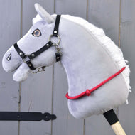 Szara pluszowa głowa Hobby Horse z czarną uzdą, metalowym wędzidłem i ręcznie wykonanym Cordeo czerwonym (rozmiar S) od Hobby Horse LarDen, osadzona na drewnianym kiju, na tle szarej drewnianej ściany.