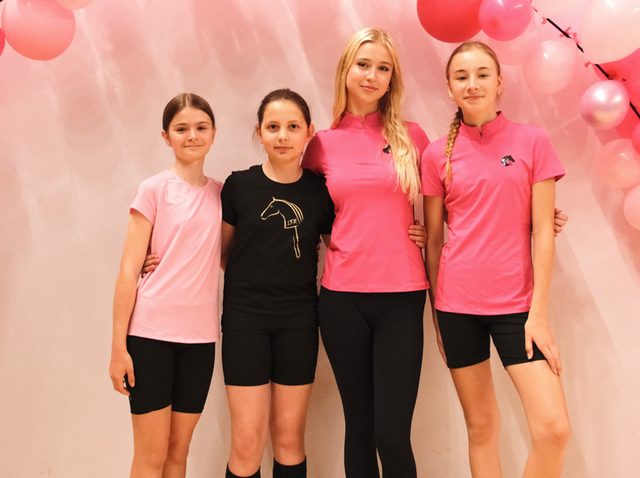Cztery młode zawodniczki stoją objęte ramionami na tle jasnoróżowej dekoracji z różowymi balonami, ubrane w sportowe różowo-czarne topy oraz czarne szorty lub legginsy, z detalami z logo Hobby Horse. Jasna, radosna aranżacja tworzy przyjazny klimat LarDen