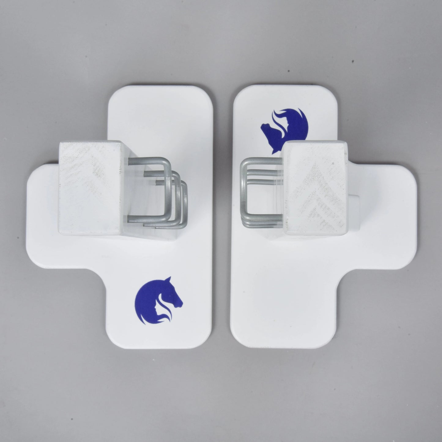 Two white cross-shaped Jump 50 cm / 20 inch obstacles by Hobby Horse LarDen, each with a blue horse head logo and central metal bracket, face each other on a gray surface—ideal for adjustable height hobby horsing jumps indoors or outdoors.