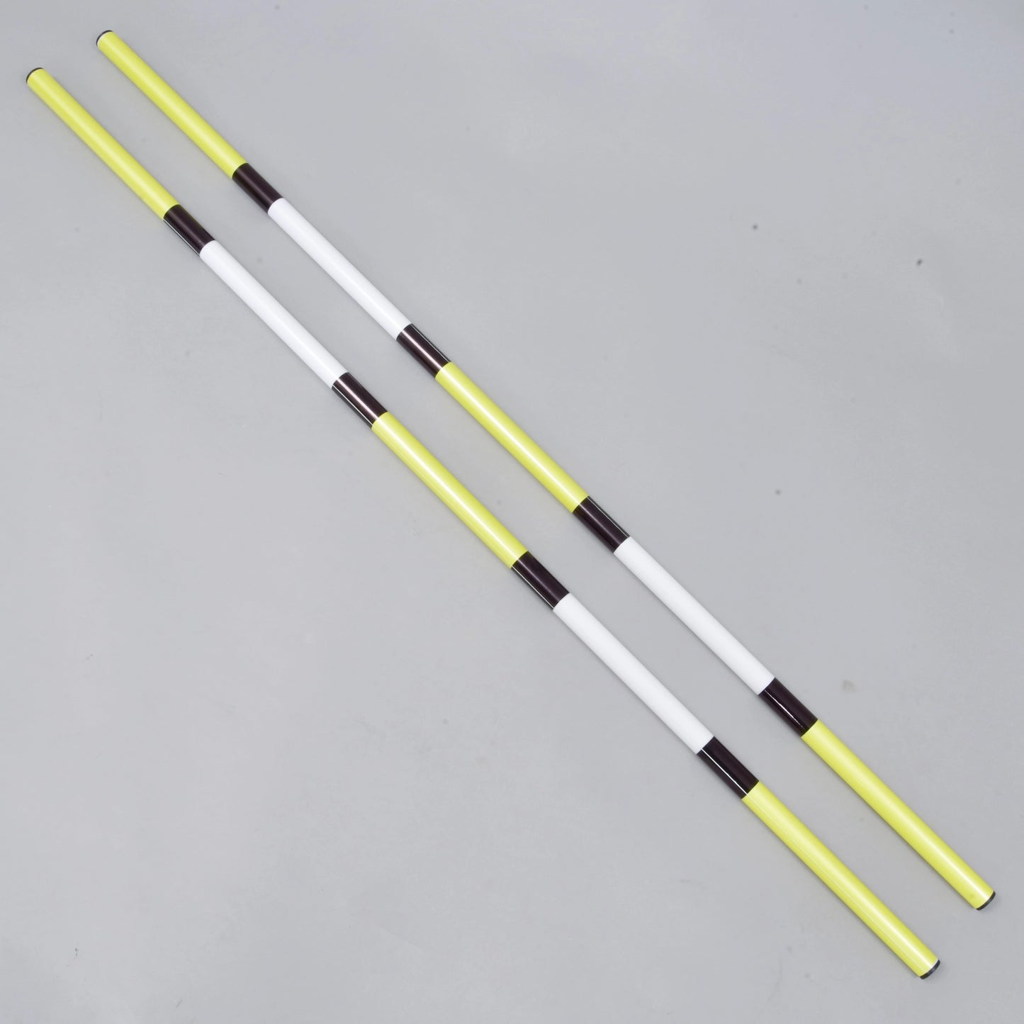 Drągi do skoków żółto-czarne 2 szt. od Hobby Horse LarDen, zestaw zawiera dwa lekkie drągi z powlekanego PVC o średnicy 32 mm z naprzemiennymi sekcjami w kolorze żółtym, białym i czarnym, pokazane równolegle na jasnoszarej powierzchni.