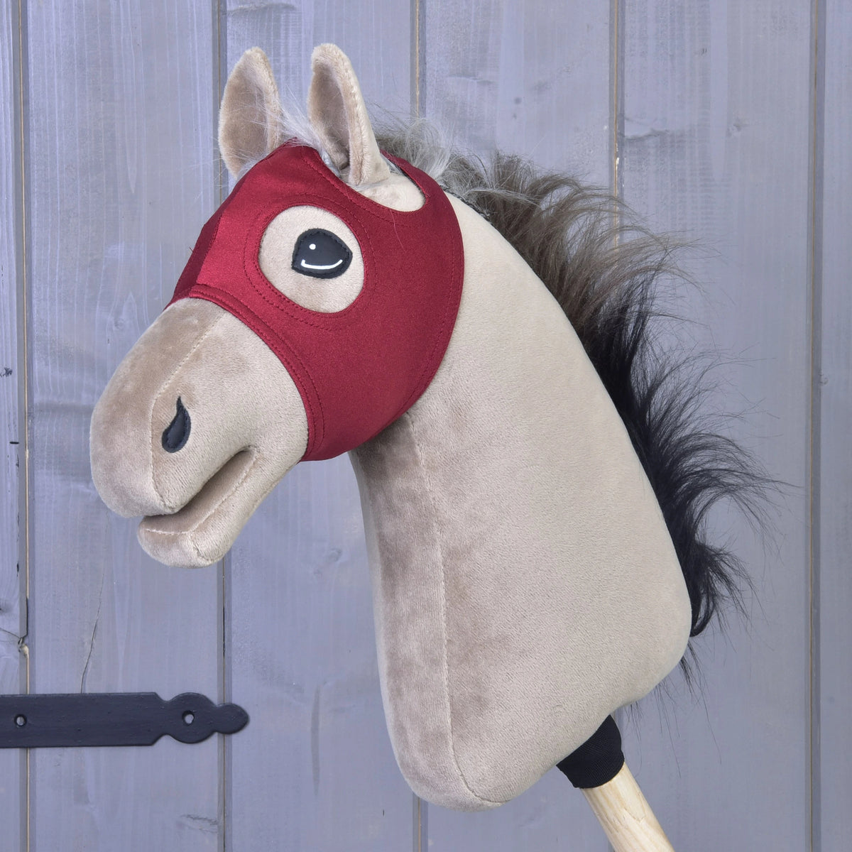Aksamitna maska na Hobby Horse bez uszu od LarDen jest zamocowana na drewnianym kiju na tle szarej drewnianej boazerii, łącząc klasyczny urok z praktycznym wykonaniem, jest to urocza zabawka nadająca się do prania, zapewniająca godziny kreatywnej zabawy i łatwą pielęgnację