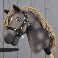 A close-up of the handmade Hobby Horse Avalon with black halter, size XS by Hobby Horse LarDen, featuring a brown coat, yarn mane, and a small white spot on its forehead. Inspired by an English Warmblood sport horse, it stands against gray wooden panels.