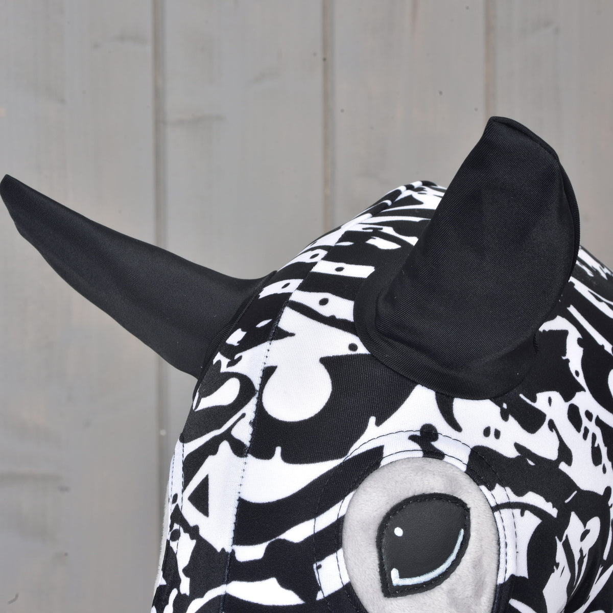 A close-up of the Hobby Horse LarDen Hobby Horse protective suit in Black & White, featuring a plush animal design with bold black ears and a large round eye, set against a light wooden background—showcasing its playful and charming patterned style.