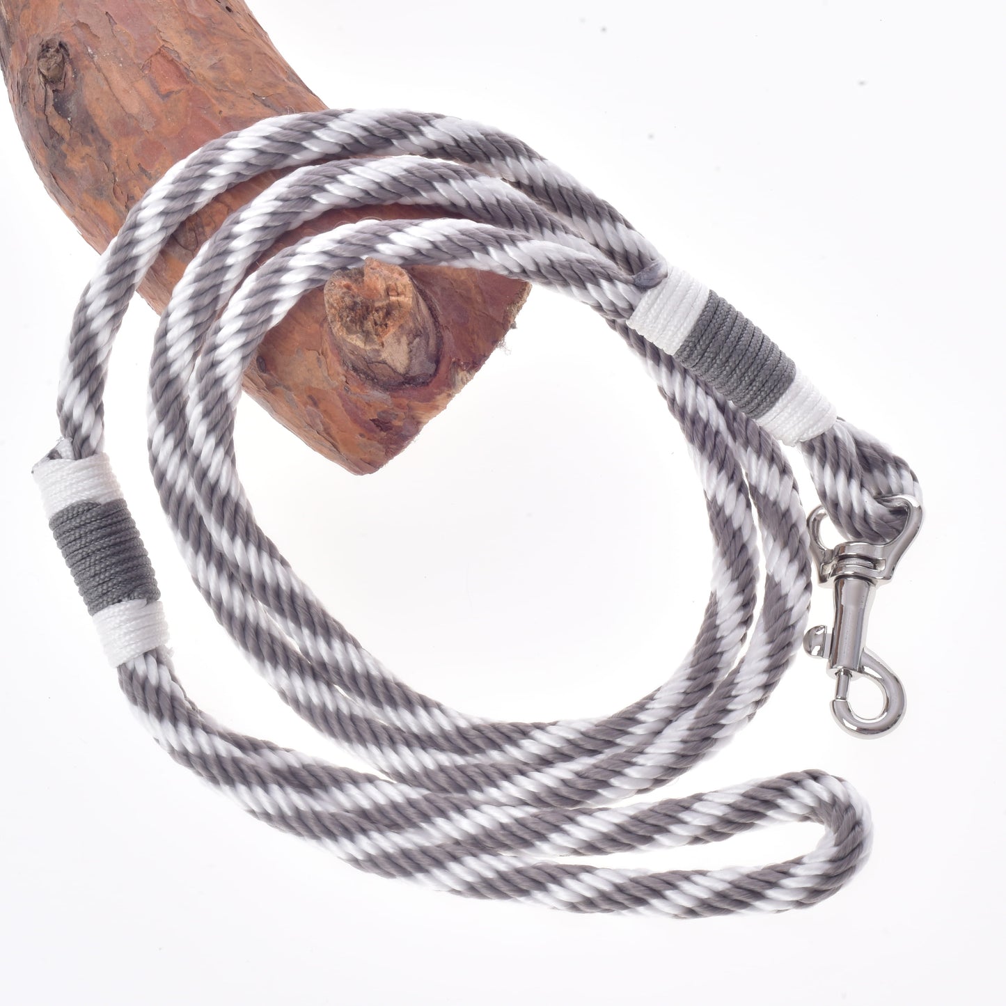The Set Start Silver by Hobby Horse LarDen—featuring a coiled black and white striped lead rope with a metal clip—rests partially looped around a wooden branch on a white background, making it perfect for use as reins, halter, or leash with your Hobby Horse accessories.