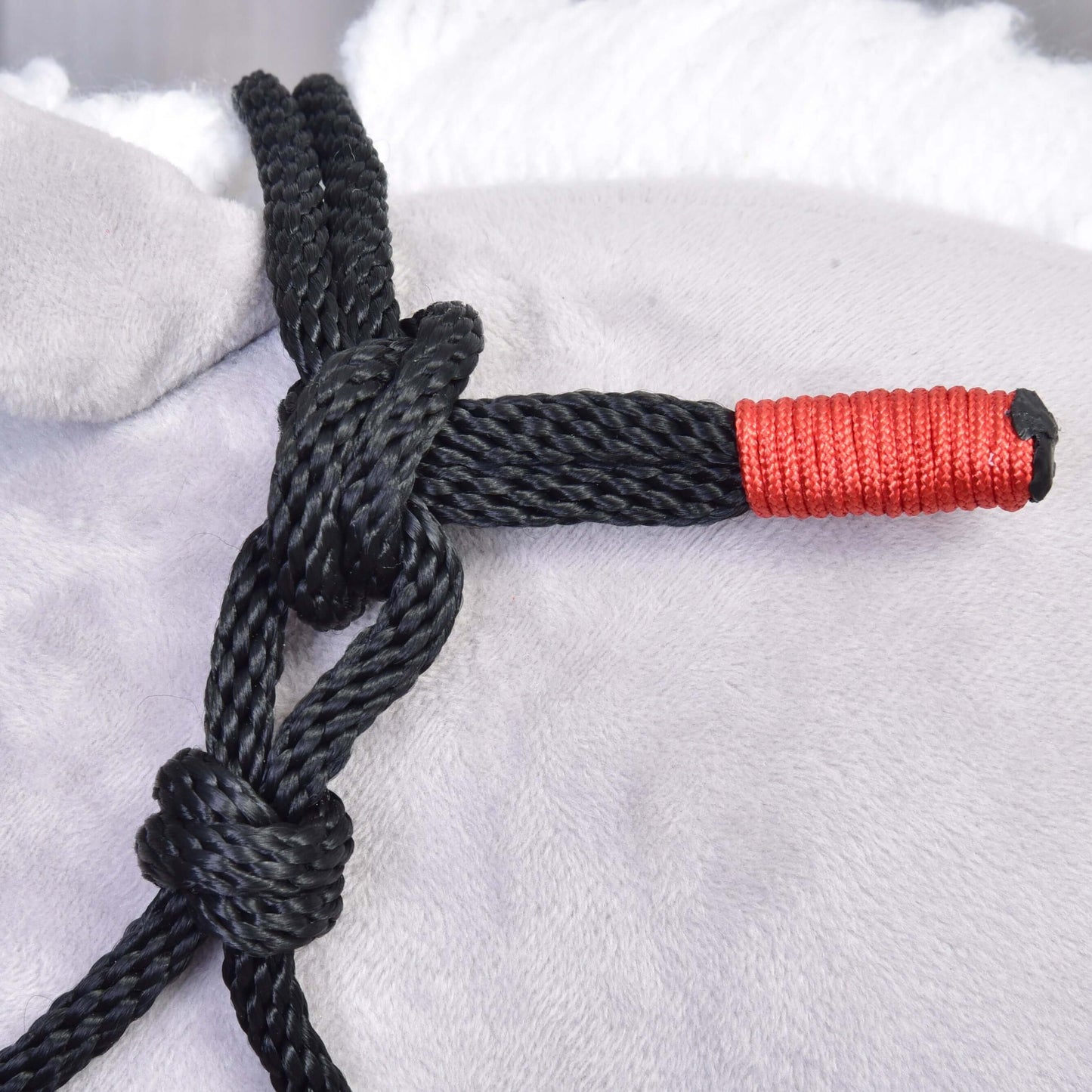 Close-up of a black polypropylene Rope set Spark by Hobby Horse LarDen, featuring two knots on light gray fabric. One end is neatly wrapped with bright red thread, enhancing this handmade accessory's unique design.