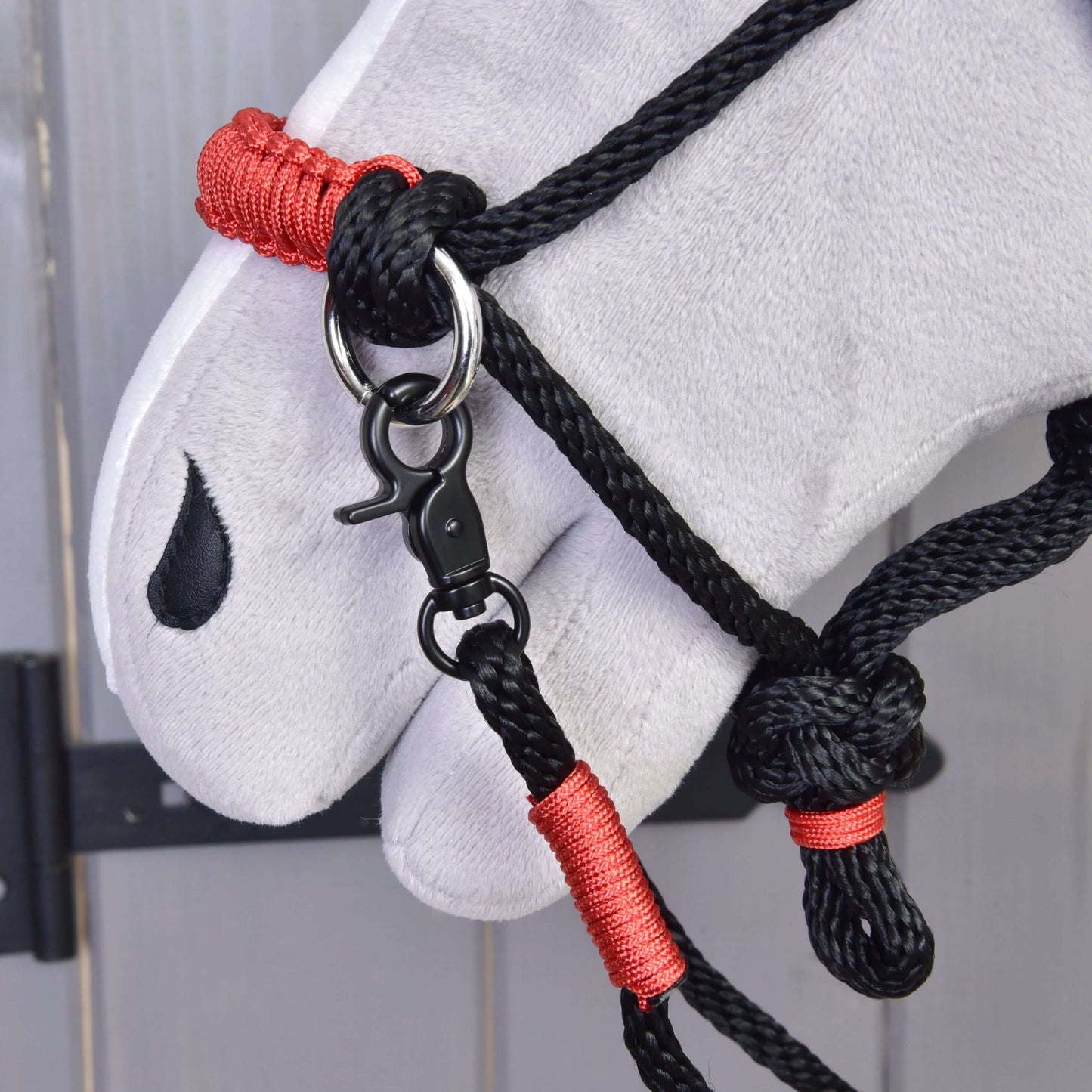 A close-up of a plush white horse’s head wearing the Hobby Horse LarDen Rope set Spark halter with red bindings and a metal clasp, featuring a black teardrop-shaped marking near its eye.