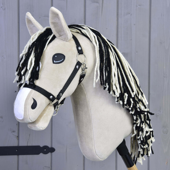 Hobby Horse Aurora z czarnym kantarem od Hobby Horse LarDen, inspirowana gniadodereszowatą klaczą, z czarno-białą grzywą z włóczki i czarnym kantarem, pokazana na tle szarej drewnianej ściany.