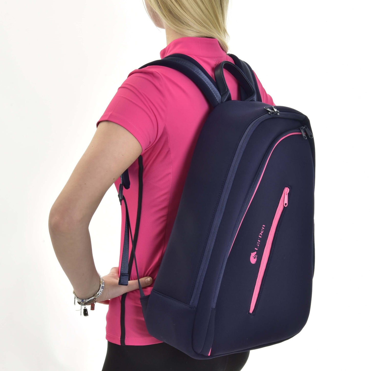 A woman in a bright pink shirt and black leggings carries the Hobby Horse Backpack LarDen by Hobby Horse LarDen, featuring padded straps and pink accents, over her shoulder as she faces away from the camera.