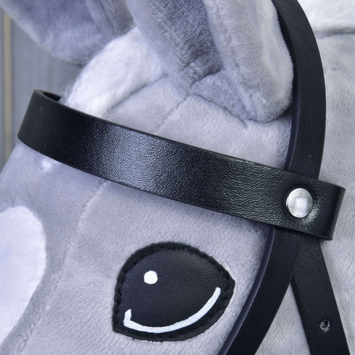 Close-up of a gray plush toy horse’s face with a Complete black bridle from leatherette by Hobby Horse LarDen, showing an embroidered black and white eye and soft, textured fabric with visible stitching.