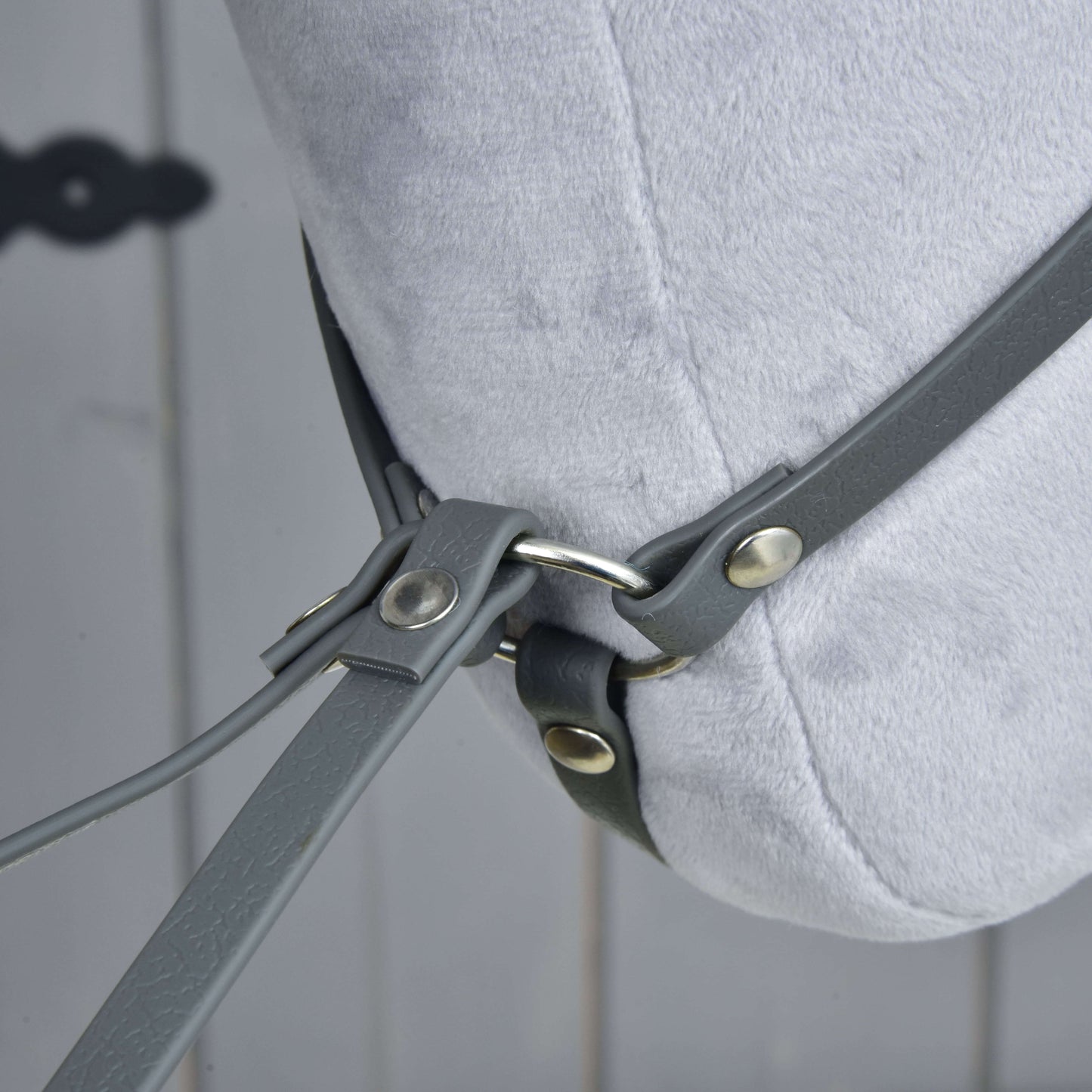 Close-up of the Martingale dark grey by Hobby Horse LarDen on a light grey plush horse head, featuring grey leather straps and metal rings against a blurred wooden background.