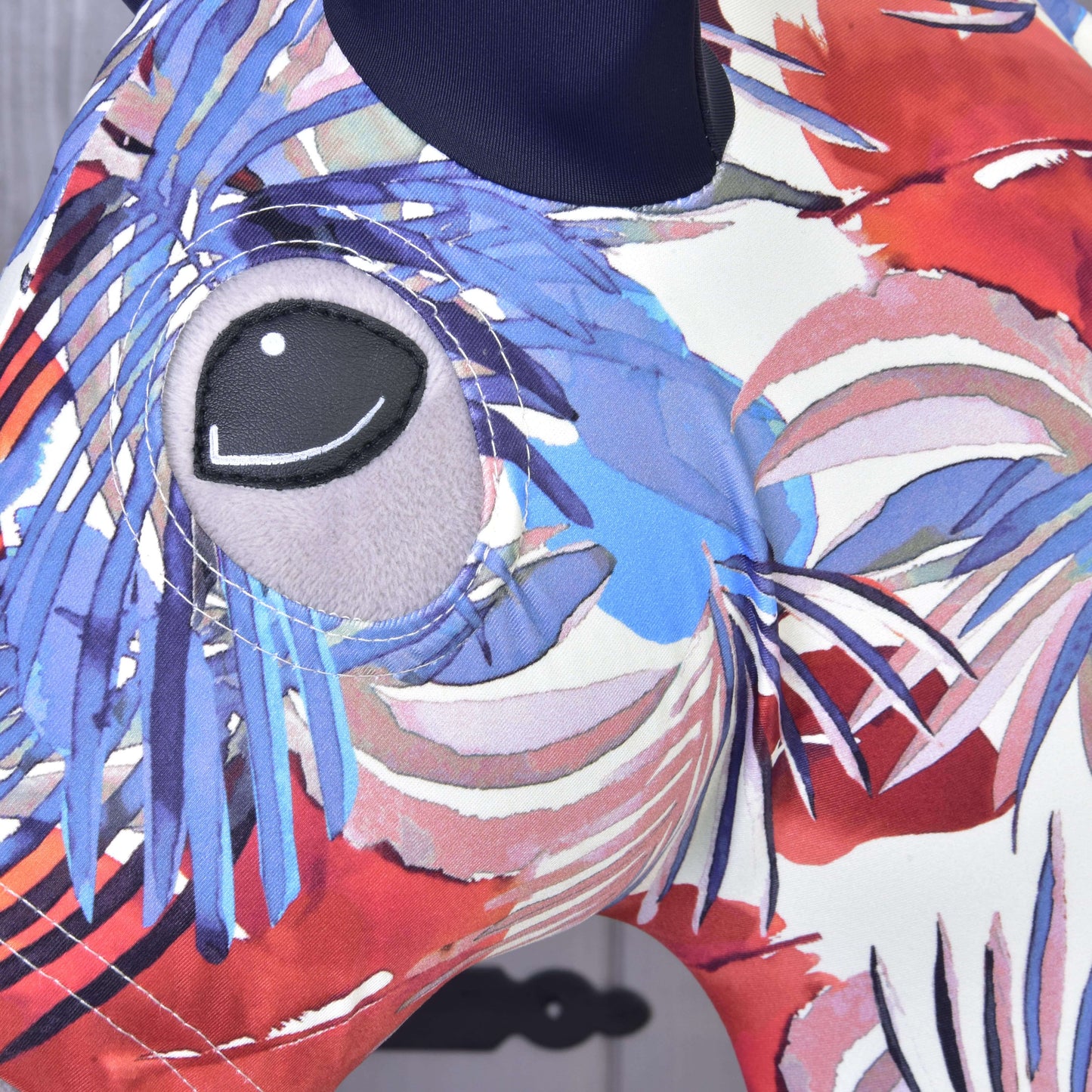 Close-up of the Hobby Horse LarDen Protective suit Blue Jungle (Lycra) featuring a colorful abstract animal design with a large gray eye and swirling patterns. The washable cover has a slightly blurred gray background, perfect for hobby horse enthusiasts.