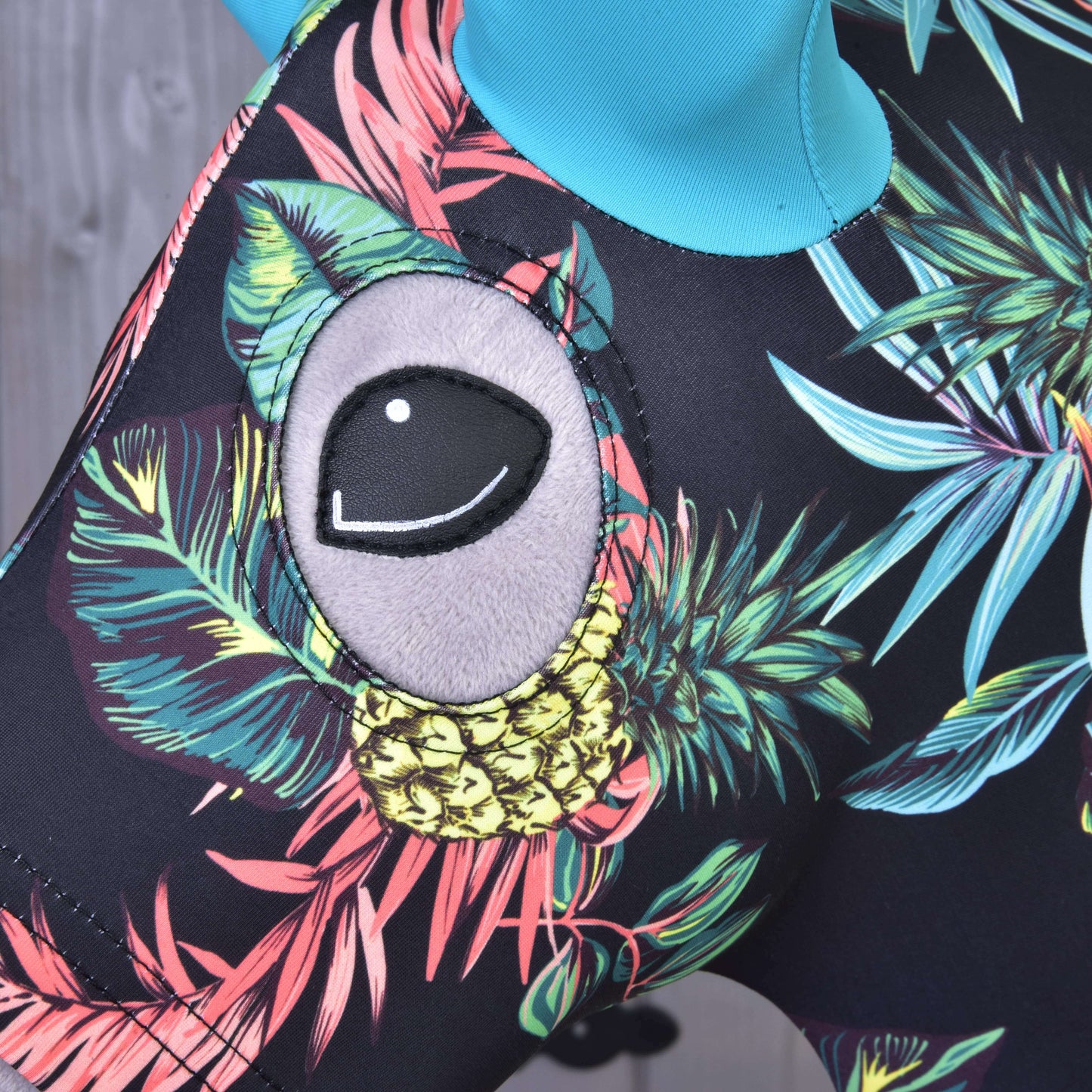 Close-up of the Hobby Horse LarDen Protective Suit Pineapple (Lycra), featuring a colorful tropical pattern with leaves, yellow pineapples, and a large cartoonish gray eye—perfect for trendy hobby horse enthusiasts.