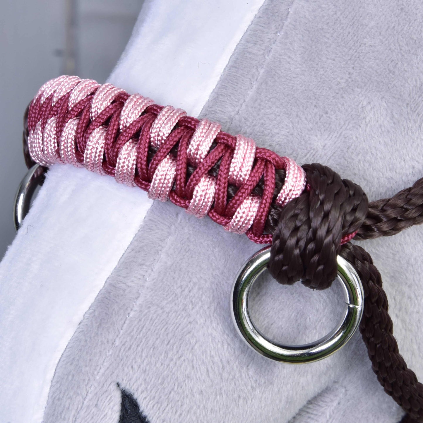 Close-up of the Rope halter York by Hobby Horse LarDen—woven pink and red band with metal rings and brown cord, resting on a soft gray surface—perfect as a stylish accessory or tack for hobby or plush horses.