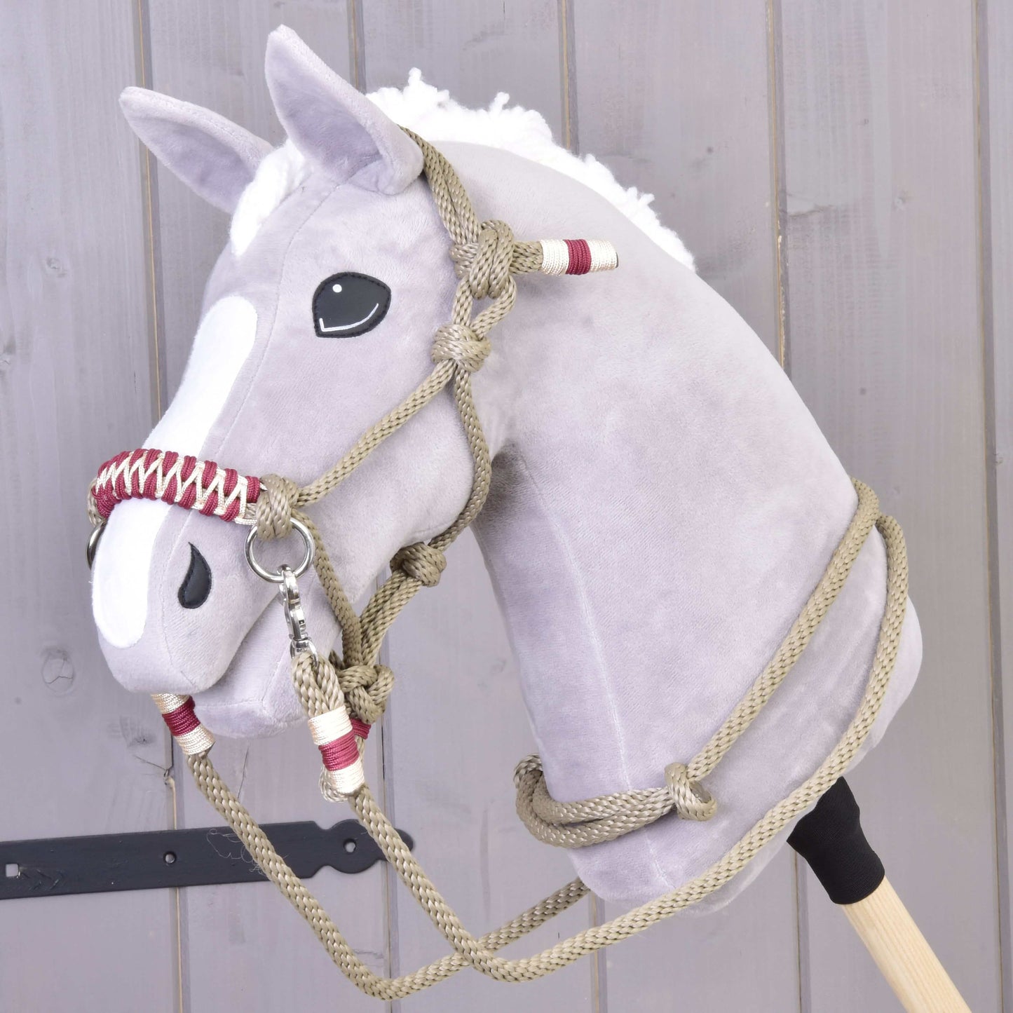 A gray plush hobby horse with a white mane and blaze, wearing the Rope set Eleganza by Hobby Horse LarDen, stands in front of a light wooden wall.