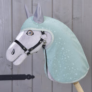 Płaszcz przeciwdeszczowy Greeny Hobby Horse LarDen na pluszowym koniu, ubranym w zielony płaszcz przeciwdeszczowy ze wzorem kropli wody i czarną uzdą, stojącym przy szarej drewnianej ścianie. Haftowane detale i stojące uszy zapewniają zabawę w każdą pogodę.