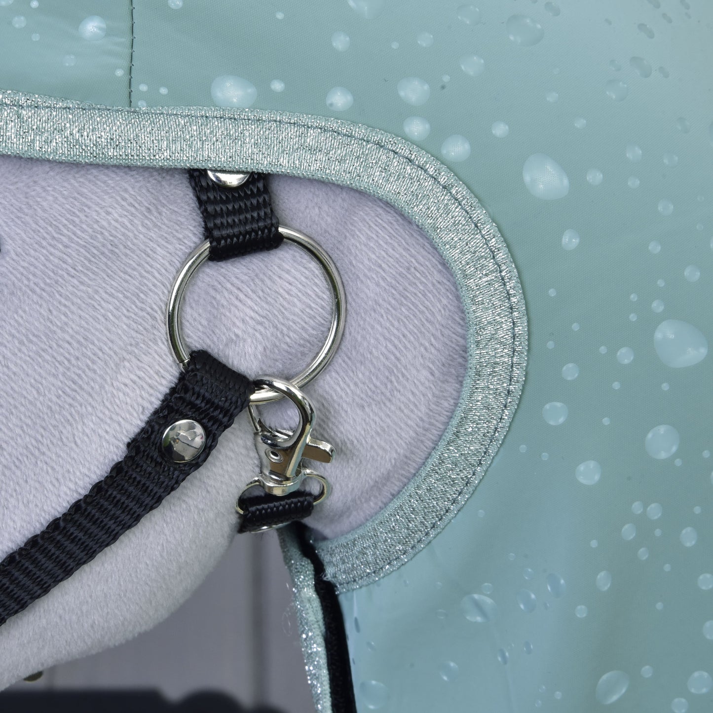 Close-up of a horse wearing the Hobby Horse LarDen Raincoat Greeny, featuring a metal ring, black strap, clip, and soft light liner with droplets—providing all-weather protection.