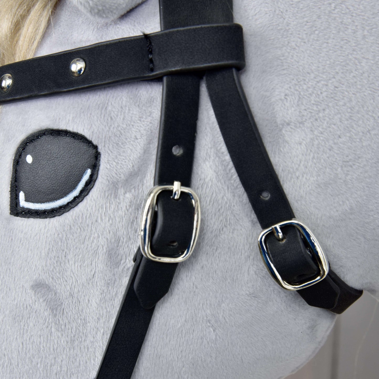 Close-up of the Hobby Horse LarDen Complete Bitless Bridle, Decorated—features soft light gray fabric, an embroidered cartoon eye, and black faux leather straps with shiny silver buckles and detachable reins.