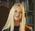 Młoda kobieta z długimi prostymi blond włosami uśmiecha się do aparatu. Ma na sobie czarną górę, a za nią widać rozmyty regał z książkami. Dłoń spoczywa delikatnie na jej ramieniu, sugerując ciepły moment po pełnym zabawy dniu z Hobby Horsing.