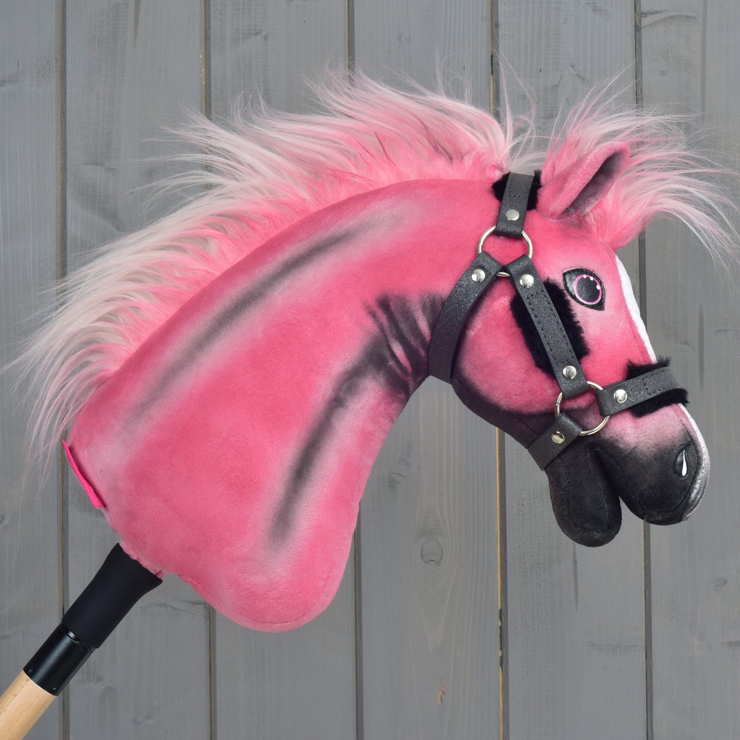 A limited edition Hobby Horse LarDen Pinkie with a glittery halter and wooden stick handle is positioned against a gray wooden panel background.