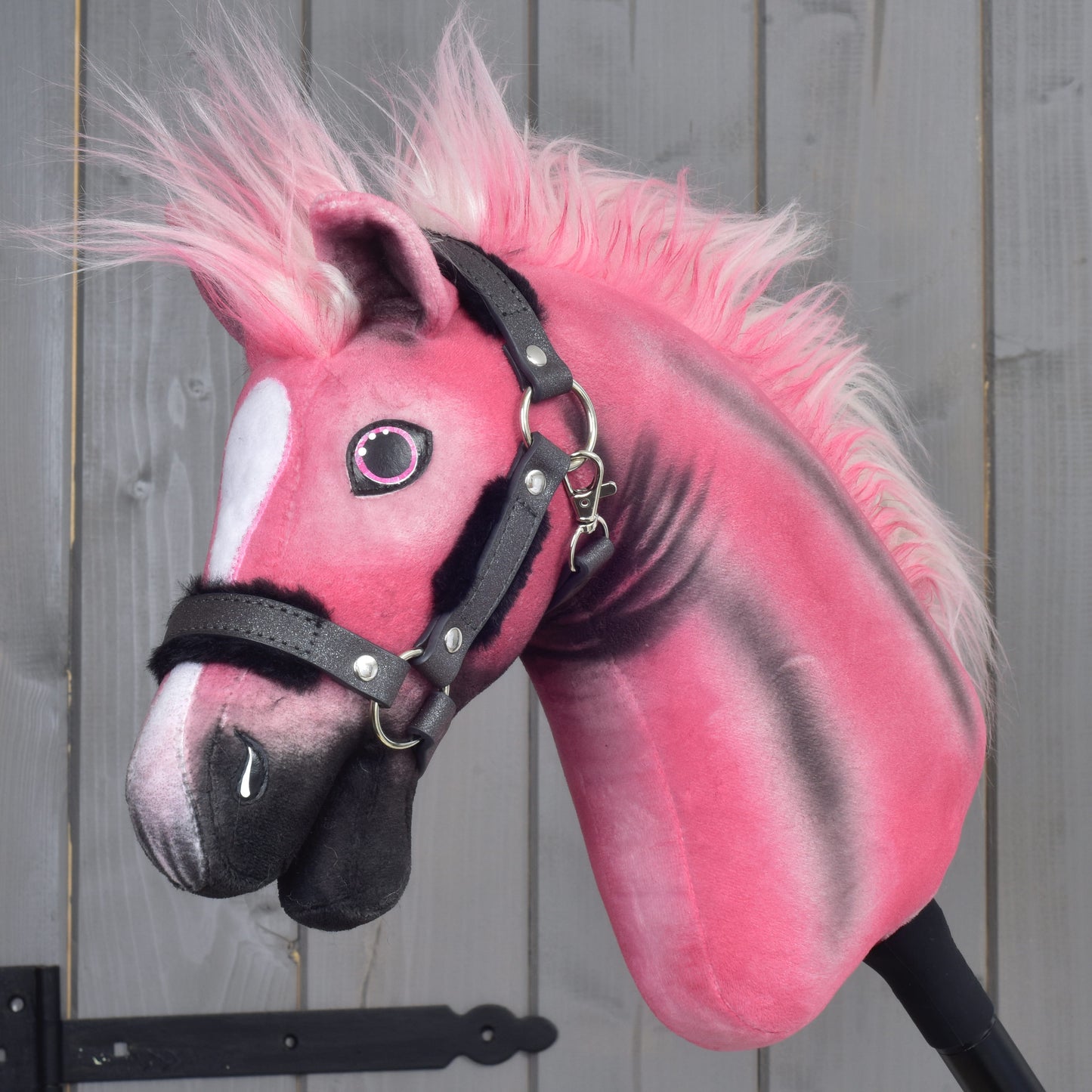A limited edition Hobby Horse LarDen Pinkie with a glittery halter, featuring a fluffy mane and a white patch on its face, is positioned in front of gray wooden panels.