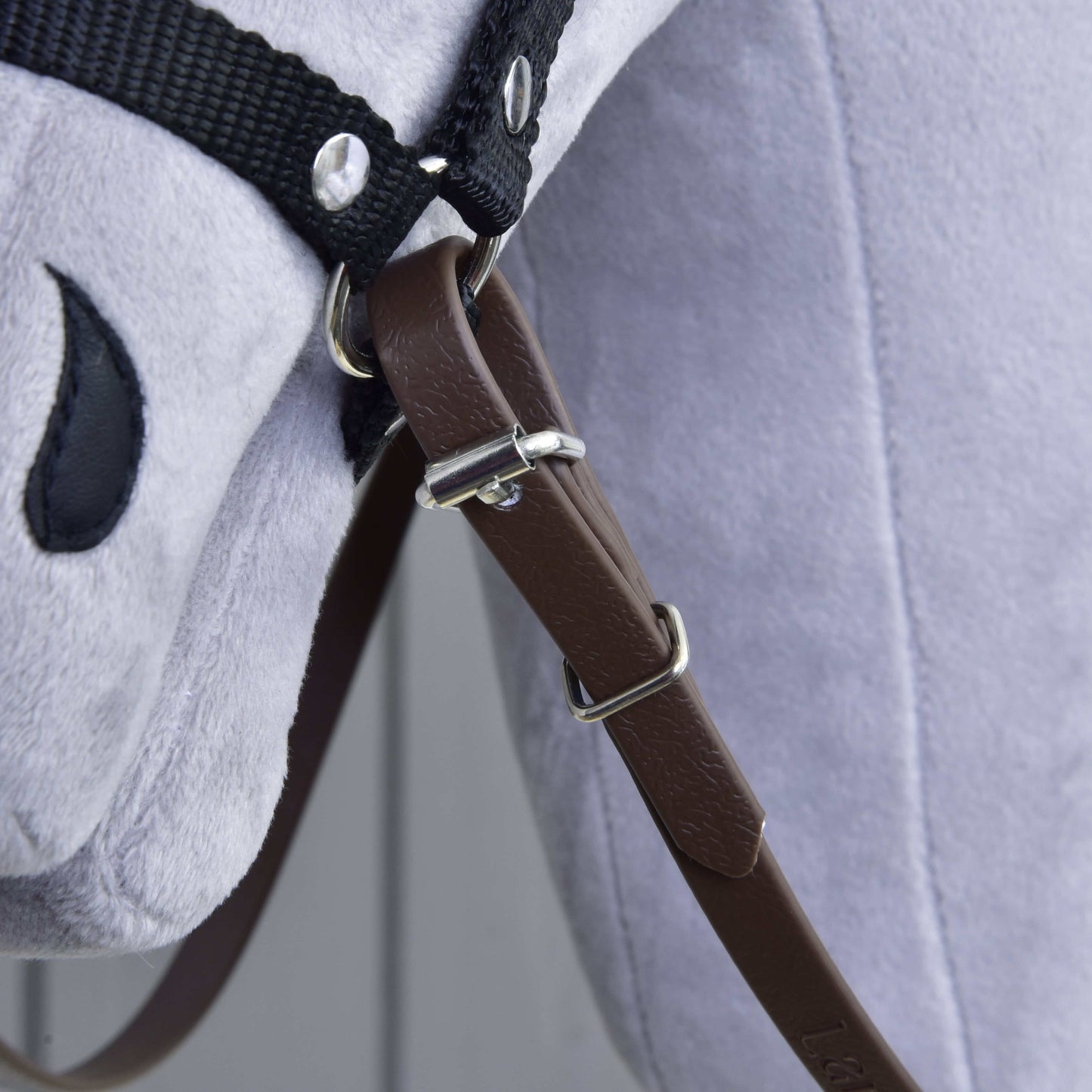 Zbliżenie na Wodze Jasnobrązowe od Hobby Horse LarDen na szarej pluszowej zabawce konia, pokazujące skórzany pasek ze sprzączką, czarne materiałowe wodze i uzdę oraz szyte czarne oko.