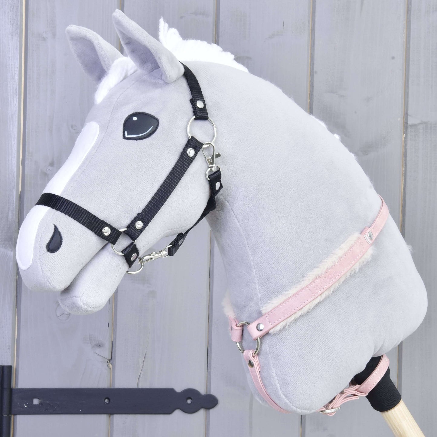 The Hobby Horse LarDen "Breastgirth with fur Mullbery" is shown: a gray plush hobby horse with white mane, black bridle, pink halter, and soft fur breastgirth on a wooden stick, set against a light gray wood background.