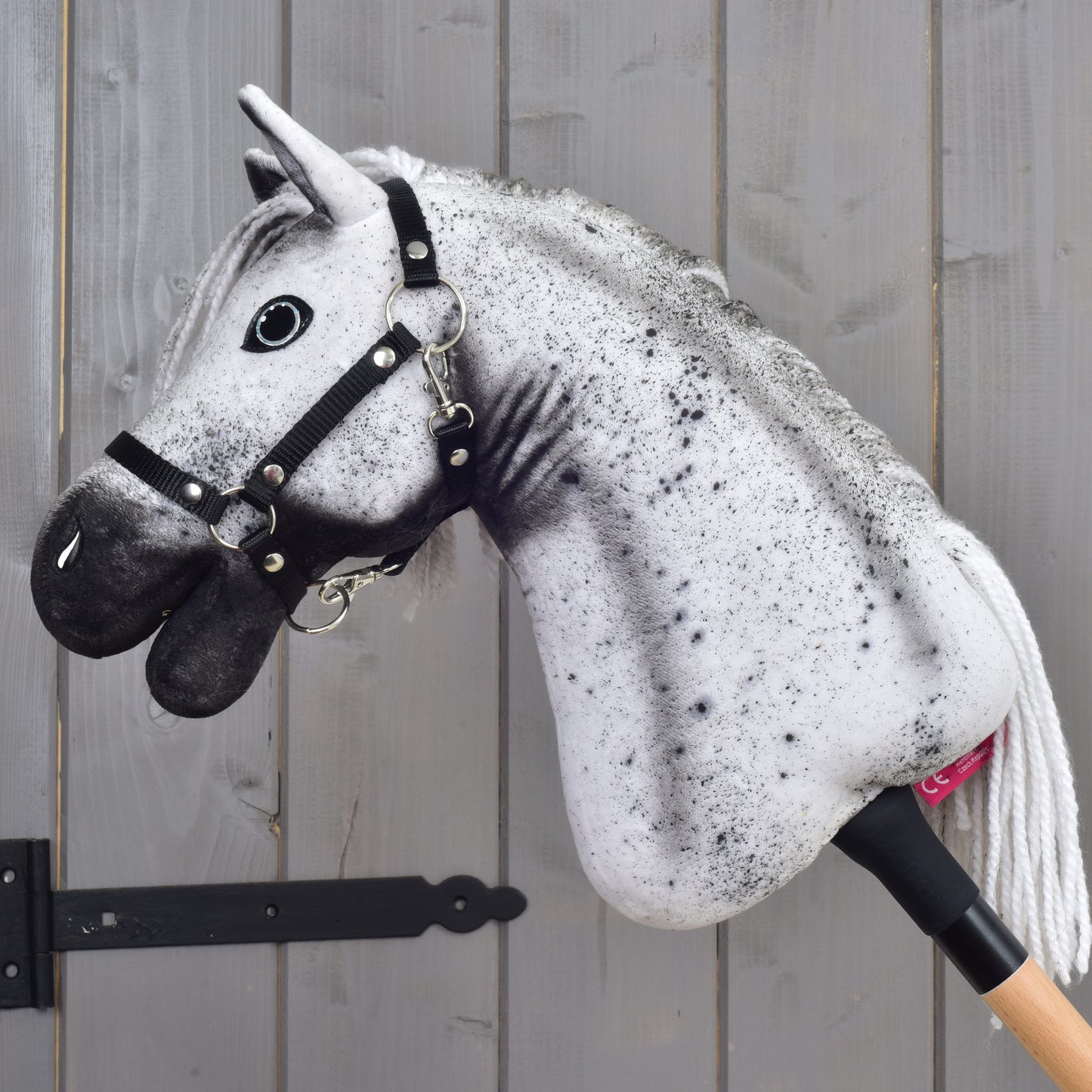 Hobby Horse Naivy z czarnym kantarem - rozmiar S od Hobby Horse LarDen, z realistyczną głową szaro-czarnego ogiera i czarnym kantarem, pokazany na tle szarej drewnianej ściany.