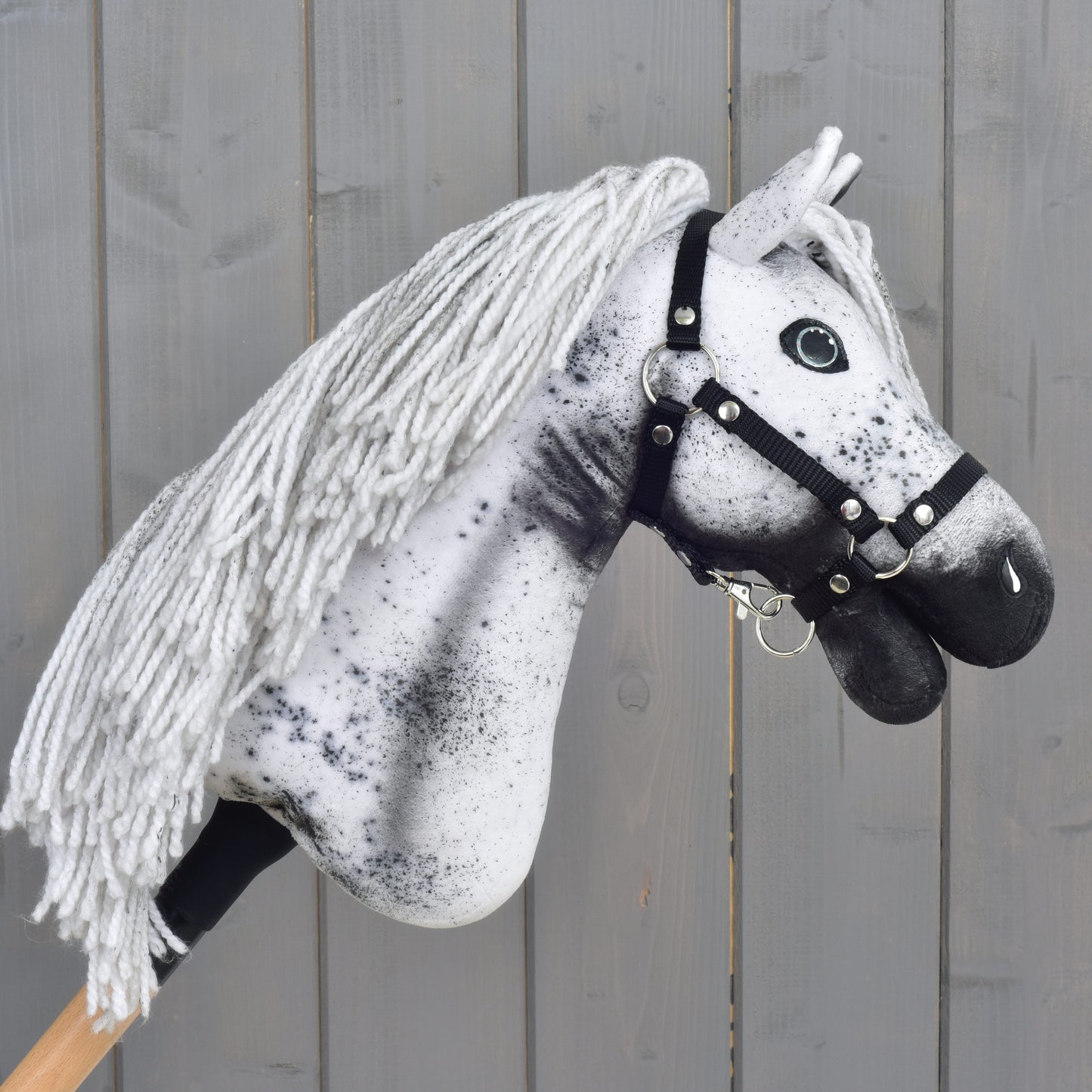Hobby Horse Naivy z czarnym kantarem - rozmiar S od Hobby Horse LarDen, ręcznie wykonany Hobby Horse Appaloosa z biało-szarą grzywą z włóczki, wyrazistymi czarnymi cętkami i czarnym kantarem, na tle rustykalnego drewnianego tła. Idealny do pomysłowych przygód z ogierem.