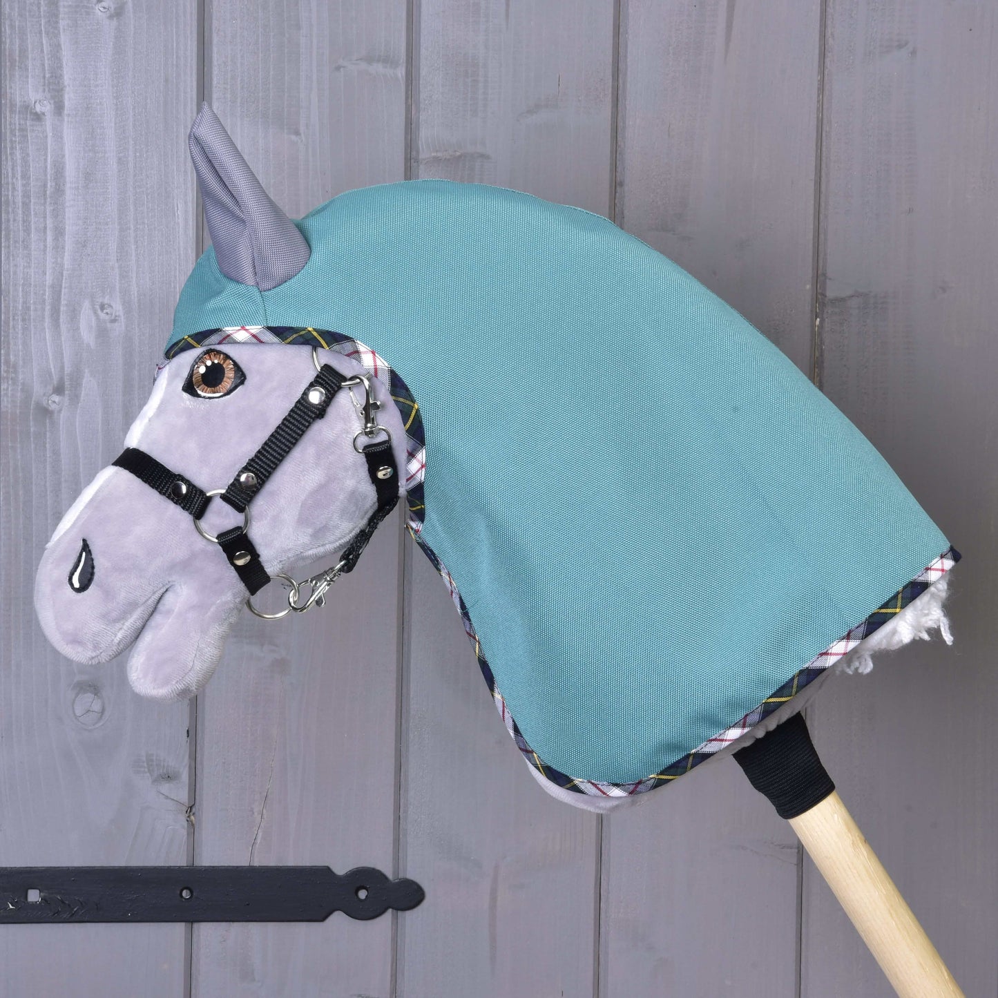 The Hobby Horse LarDen Summer raincoat Emerald is displayed on a wooden stick, featuring an emerald green softshell hood and stylish details, set against a gray wooden wall.