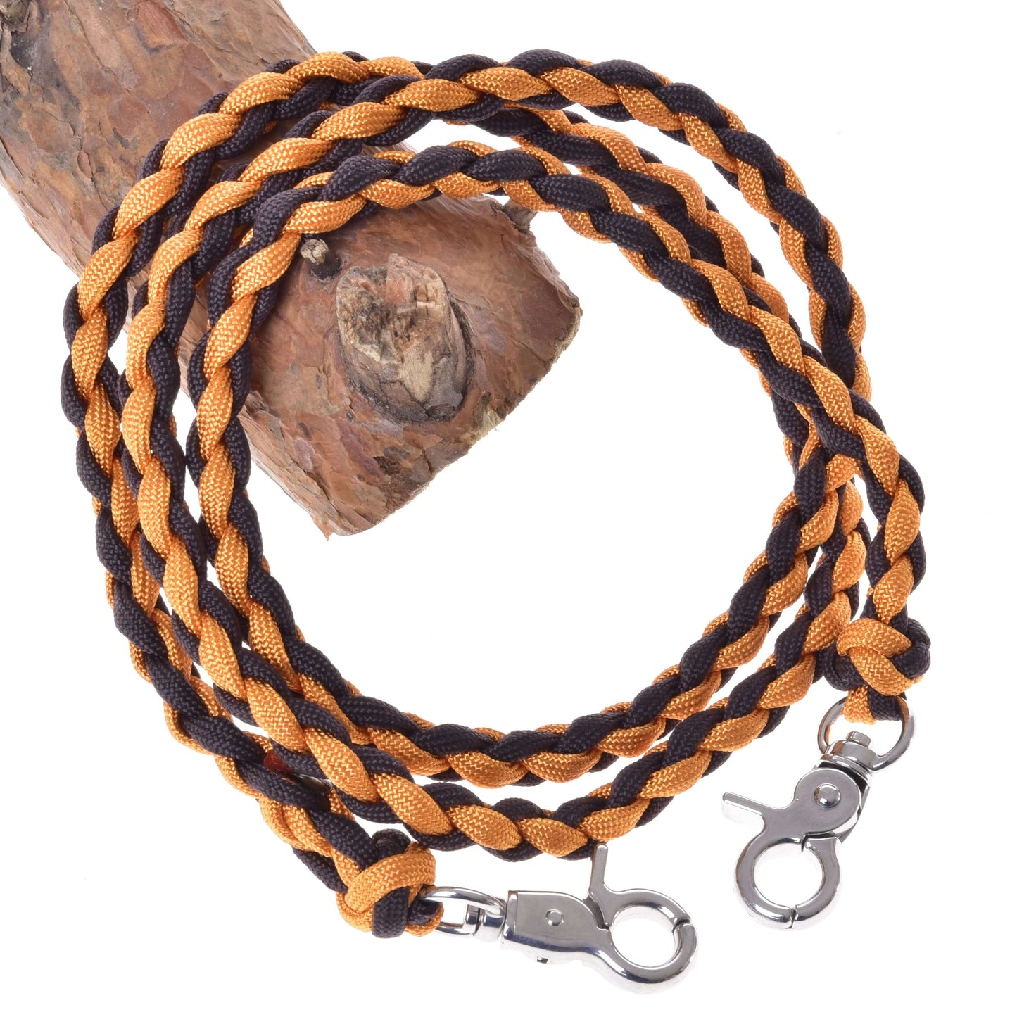 The Reins Knitted Pomello by Hobby Horse LarDen is a coiled, braided brown and black polypropylene rope with silver metal clasps on each end, shown draped over a tree branch.