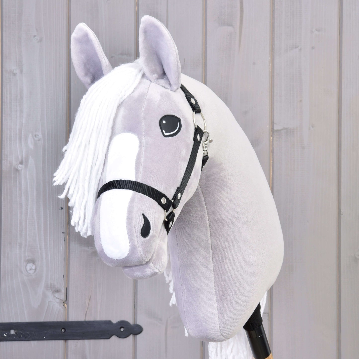 The Hobby Horse LarDen Hobby Horse Popcorn with Black Halter features a gray plush design, white mane, and friendly face—a perfect companion for imaginative play. Shown here standing before a light wooden wall.