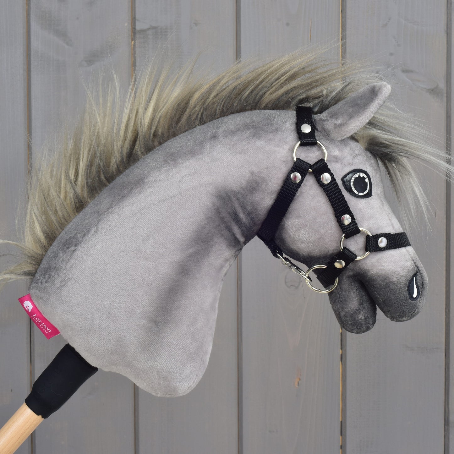 Hobby Horse LarDen’s Hobby Horse Prestige with black halter, size XS, features a soft gray design inspired by an English Warmblood and includes a realistic mane and black halter. Mounted on a wooden stick and photographed against a light wooden panel background, it’s perfect for young riders dreaming of show jumping fun.