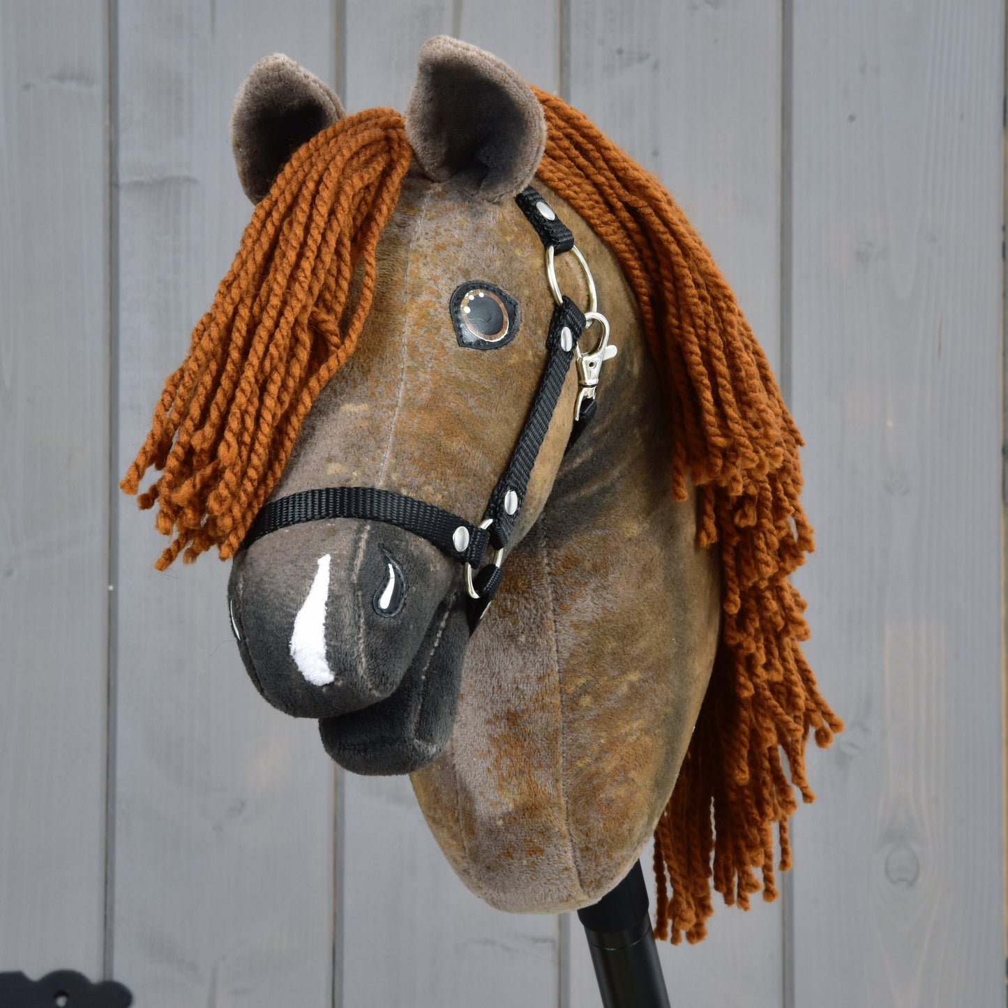 The Hobby Horse LarDen Rafaello with Black Halter (size S) features brown plush fabric, glassy eyes, a thick orange-brown yarn mane, and is photographed against a light wooden background.
