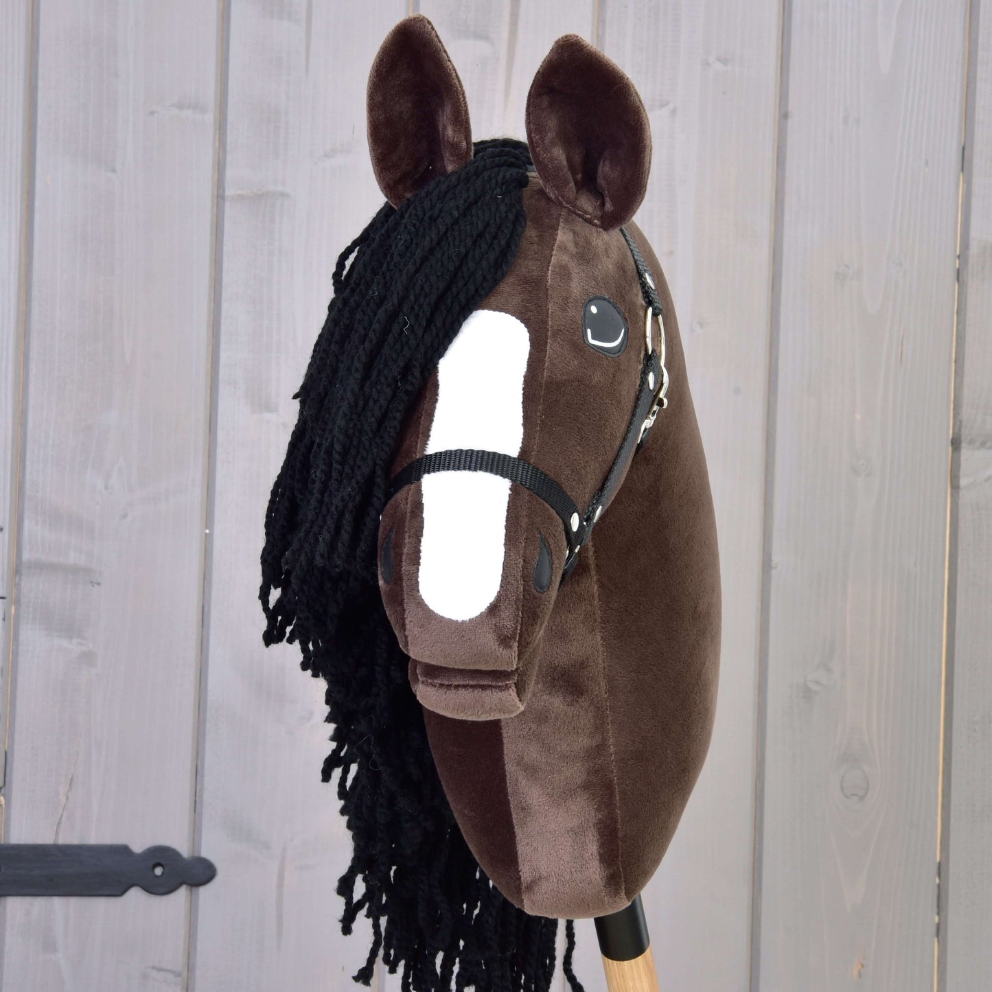 The Hobby Horse LarDen "Hobby Horse Sisi with Black Halter" features a dark brown face, white snout marking, black yarn mane, and bridle, capturing the elegance of a Hanoverian sport horse against a light wooden background.