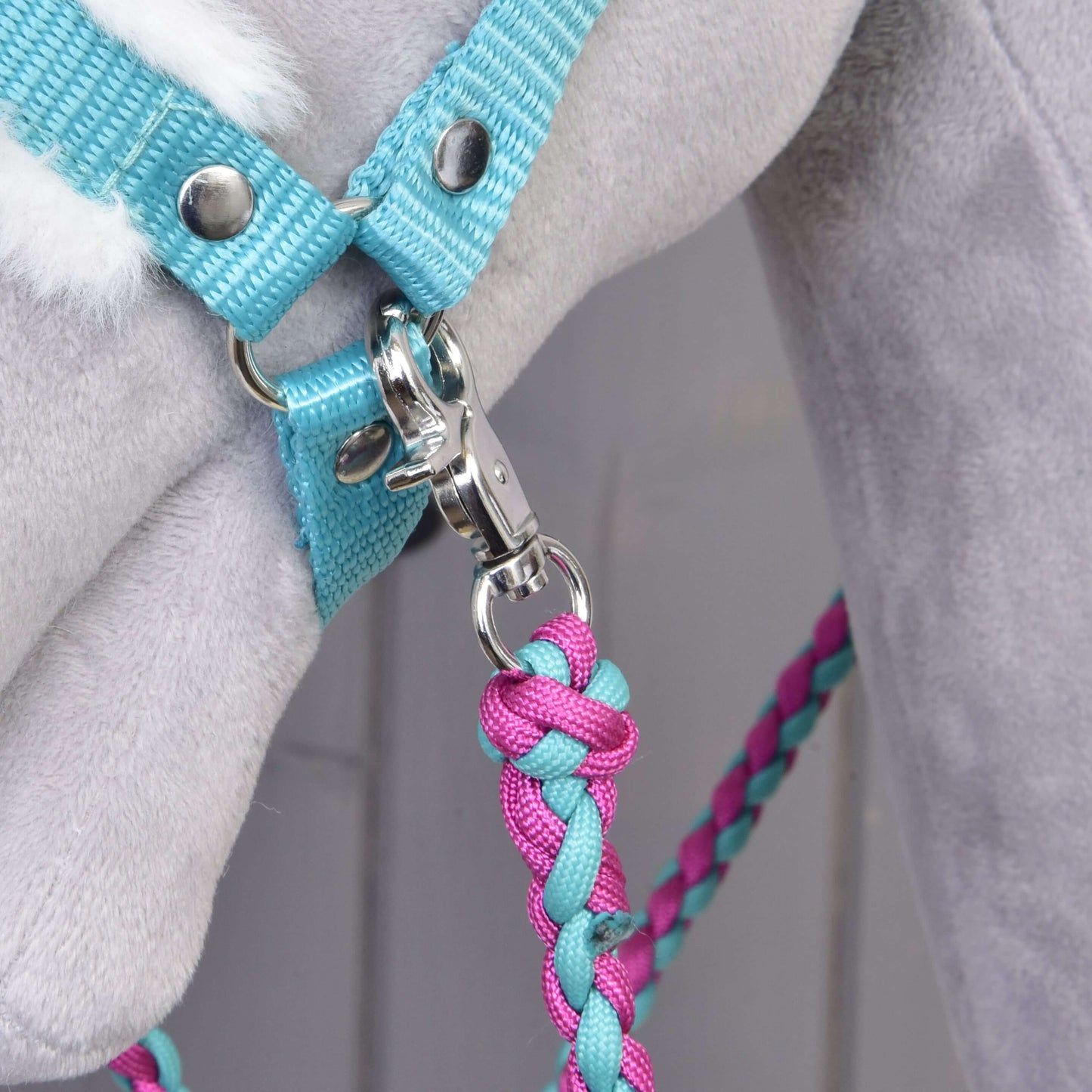 Close-up of the Set Perfect Combination Turquoise by Hobby Horse LarDen, featuring a braided pink and blue lead rope clipped to a turquoise fur-padded halter on a light grey plush horse—ideal for hobby horse accessories fans.