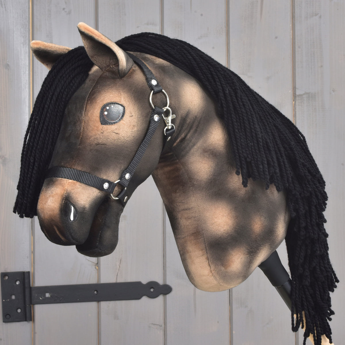 Hobby Horse LarDen „Stormy” ma brązową pluszową głowę, czarną włóczkową grzywę, czarny kantar i błyszczące guzikowe oczy, osadzone na drewnianym kiju na tle jasnego drewna — urzekający model inspirowany duchem ogiera hanowerskiego.