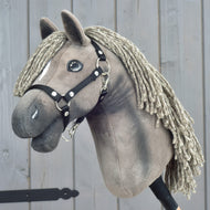 Hobby Horse Swing z czarnym kantarem, rozmiar S od Hobby Horse LarDen, z pluszowym koniem, plecioną grzywą z włóczki i eleganckim czarnym kantarem, osadzony na kiju i pokazany na drewnianym tle.