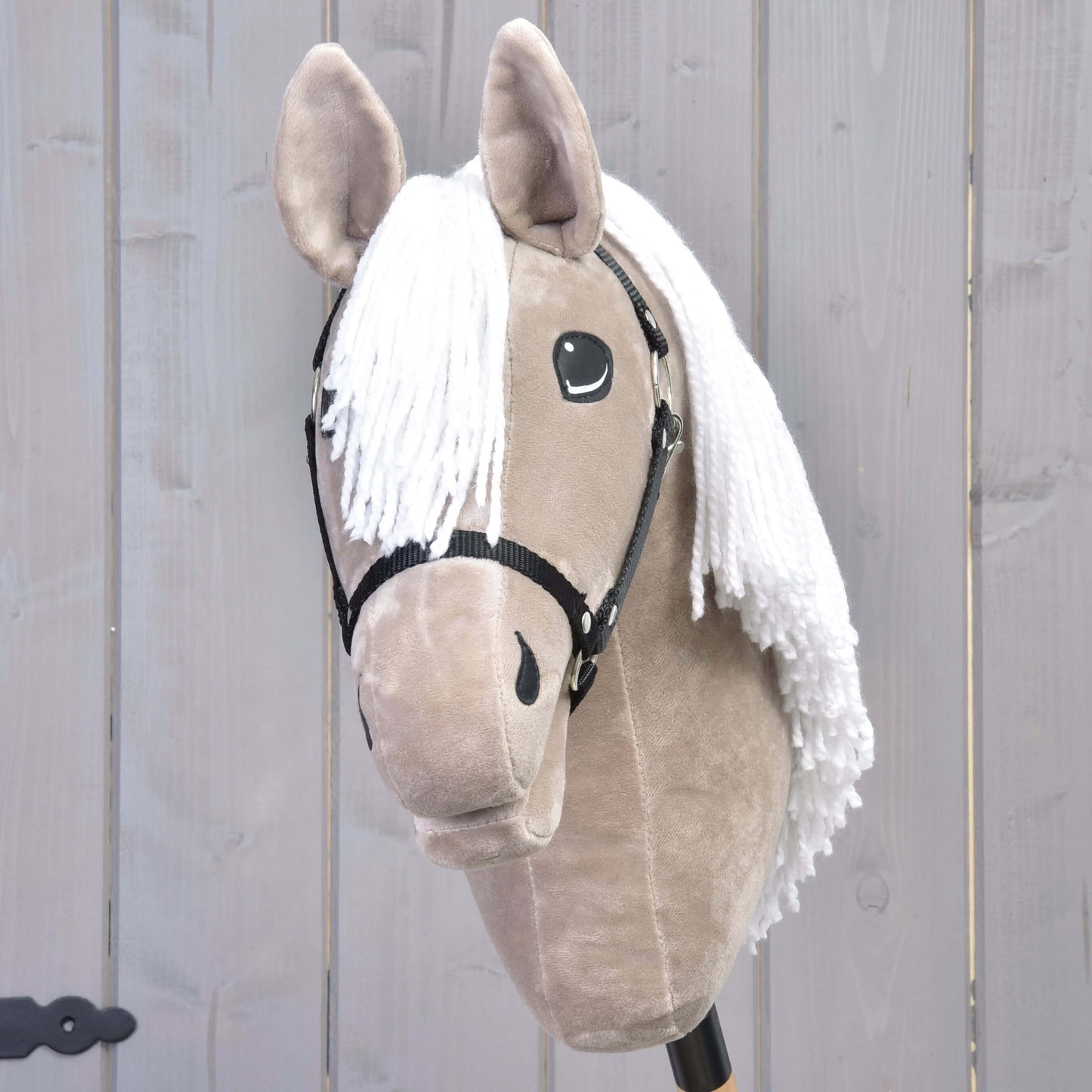 The Hobby Horse LarDen "Hobby Horse Blondie with Black Halter" features a light brown head, black button eyes, white yarn mane, and black halter, inspired by the American Quarter Horse, in front of a light gray wooden wall.