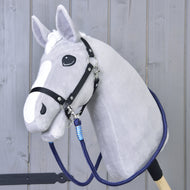 Reins Blues od Hobby Horse LarDen, szary pluszowy Hobby Horse z czarną uzdą, ręcznie robionymi wodzami, niebieskim uwiązem i białymi znaczeniami na pysku, na drewnianym kiju, pokazany na tle szarej drewnianej ściany.