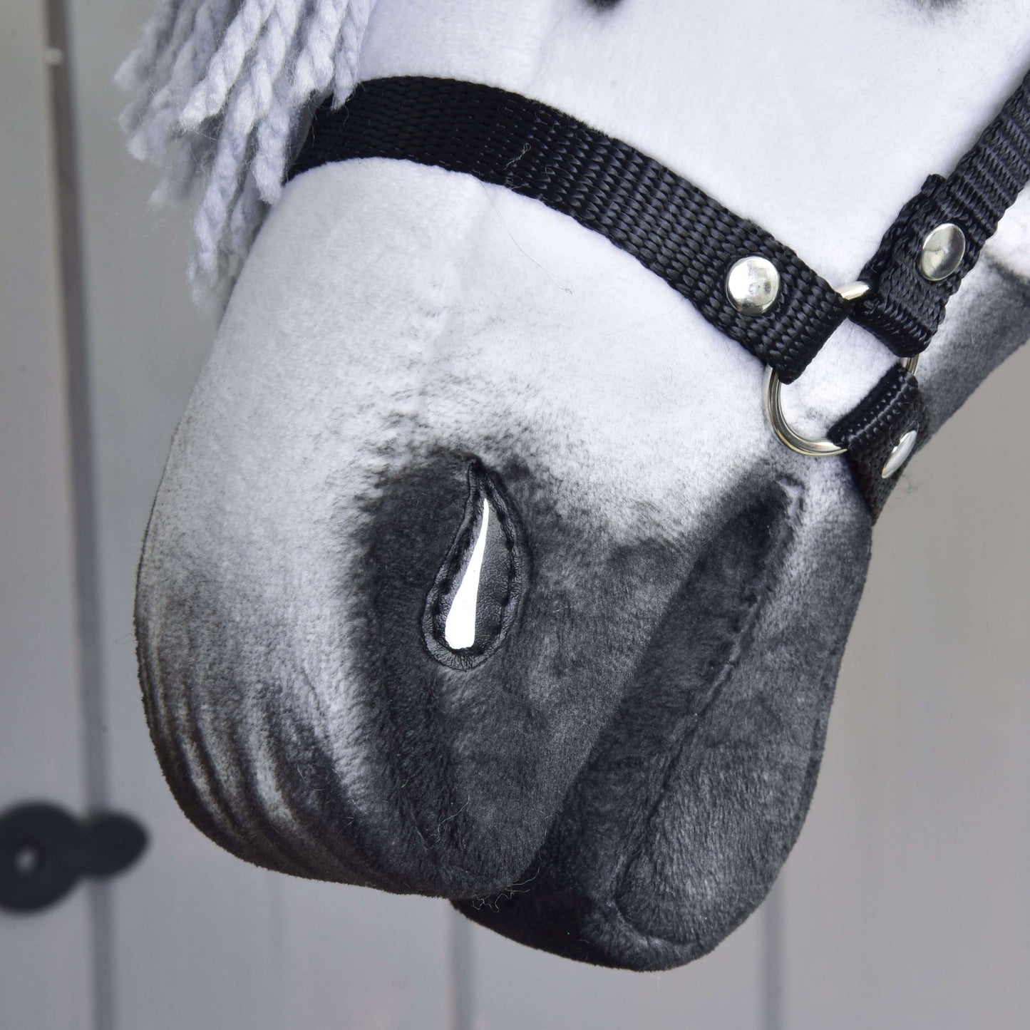 Close-up of Hobby Horse LarDen’s handmade Hobby Horse Chantal with a black halter, white and gray coloring, painted teardrop detail, yarn mane, and neutral background.