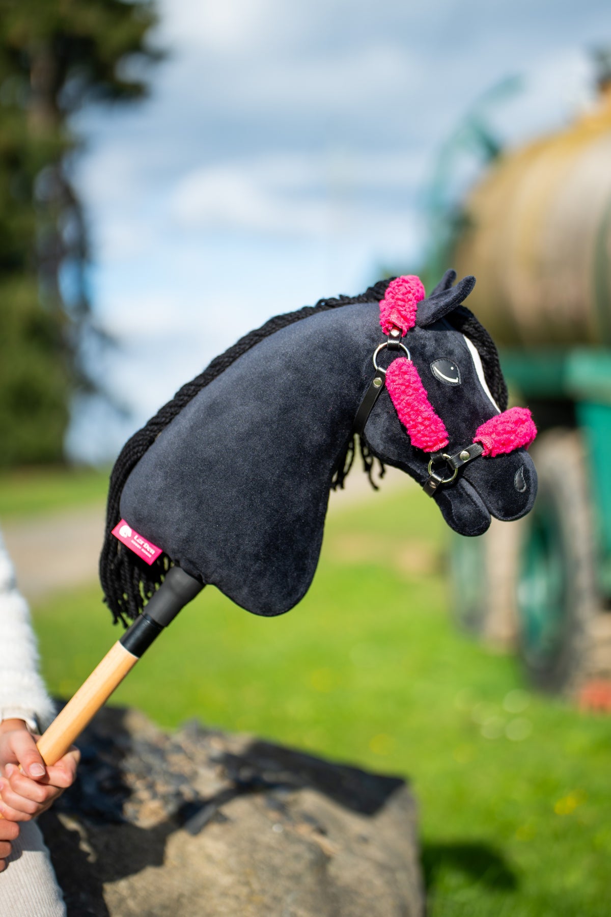 Detail photo: the head and neck of the Hobby Horse Cloony with Black Halter by Hobby Horse LarDen held up against a cloudy sky - black plush, white star, black yarn mane - shown here with the black leatherette halter with complete pink fur.
