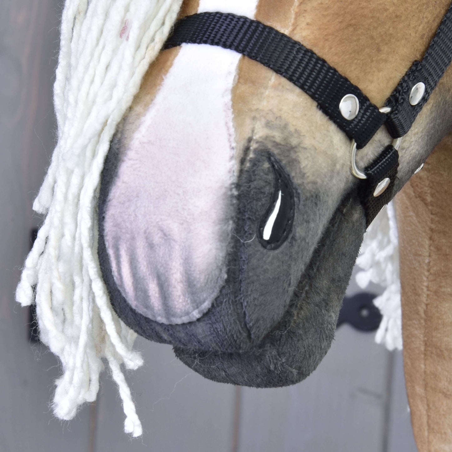 Zbliżenie na ręcznie wykonaną Connie od Hobby Horse LarDen, z jasnobrązowo-białym pyskiem, czarnym kantarem i białą grzywą z włóczki. Widoczne są szczegółowe szwy i faktura tkaniny.
