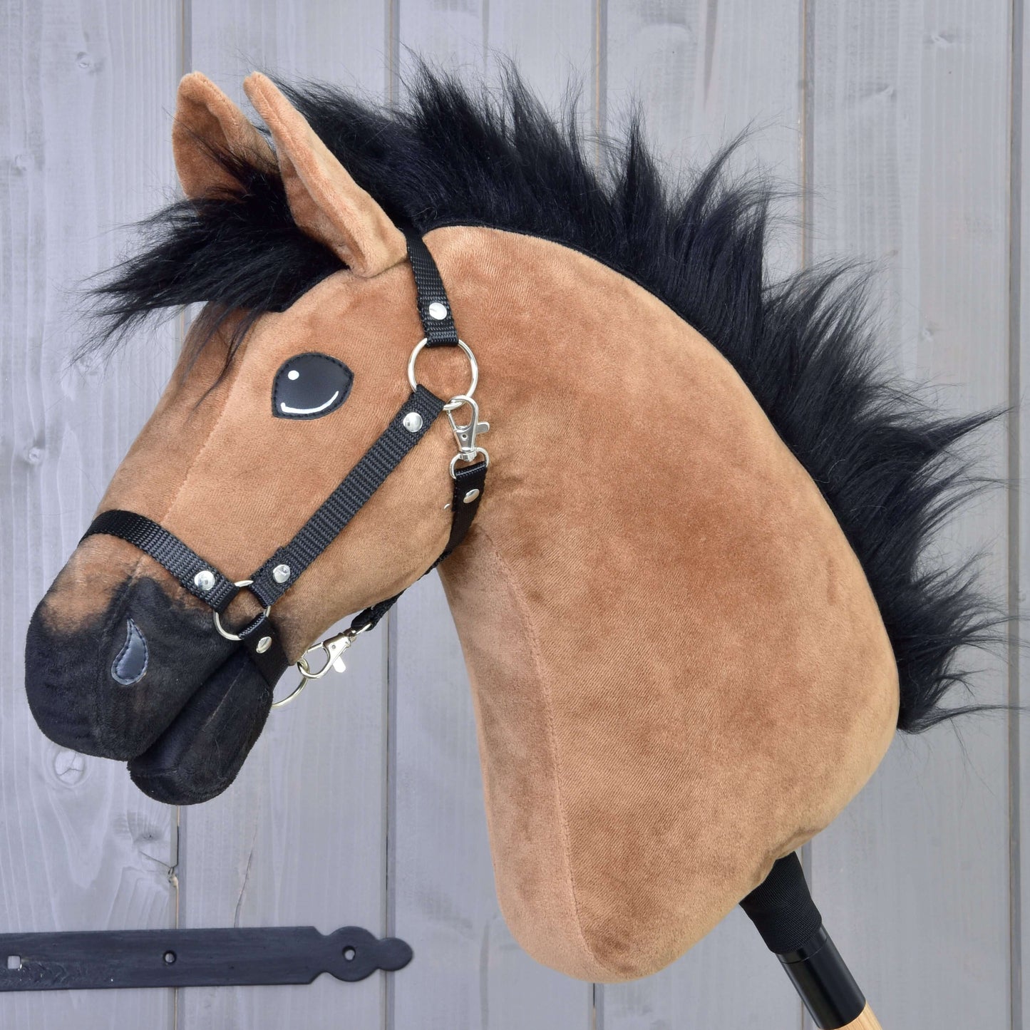 A close-up of the Hobby Horse Cookie with Black Halter by Hobby Horse LarDen, featuring a brown plush horse with a black mane and halter, shiny eyes, and a gray wooden background.
