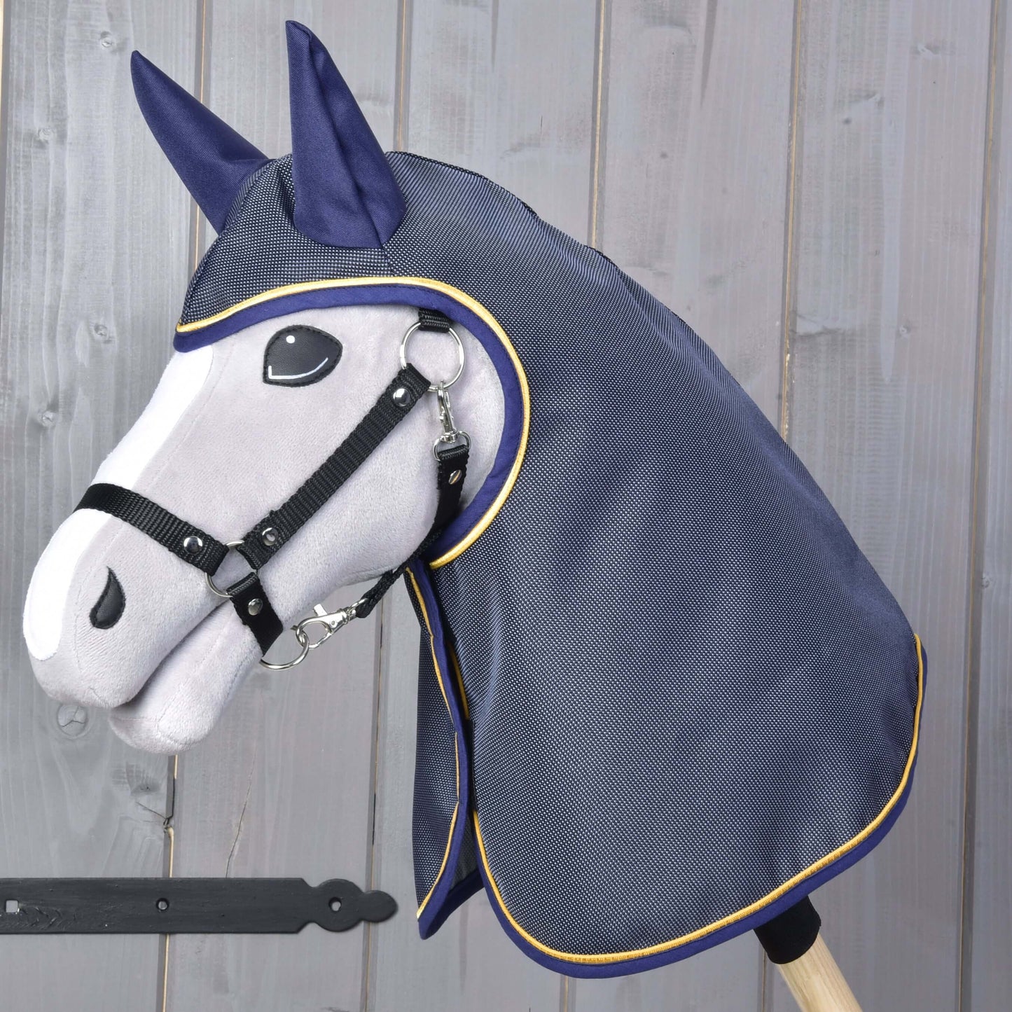 The Hobby Horse LarDen "Raincoat Crone" features a plush gray stick horse head with black bridle and a navy blue raincoat with yellow trim, shown against a wooden background.